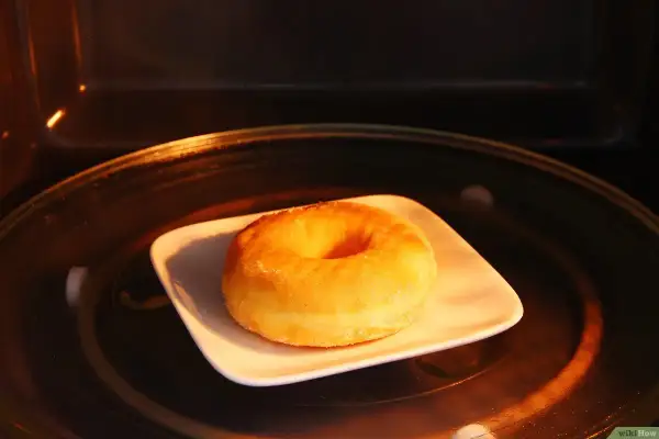 Ein einzelner Donut auf einem weißen Teller in einem Mikrowellenofen. So bleiben Donuts frisch.