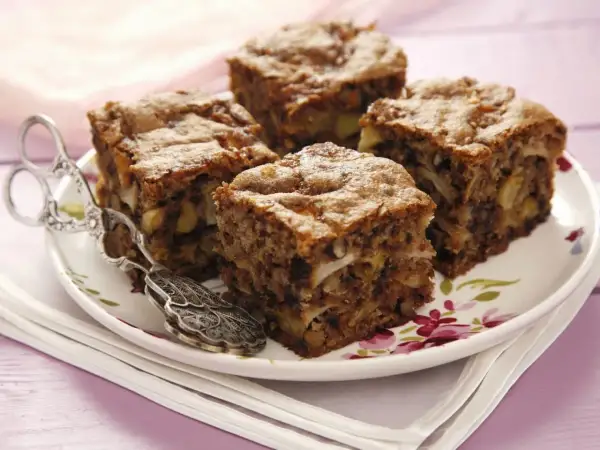 Vier Stücke saftiger Apfel Walnuss Kuchen auf einem Teller mit floralem Muster, daneben eine antike Kuchenzange.