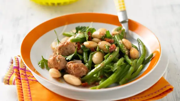 Bohnensalat rezept: Frischer Bohnensalat mit weißen Bohnen, grünen Bohnen, Thunfisch und Kräutern auf einem Teller mit orangem Rand.
