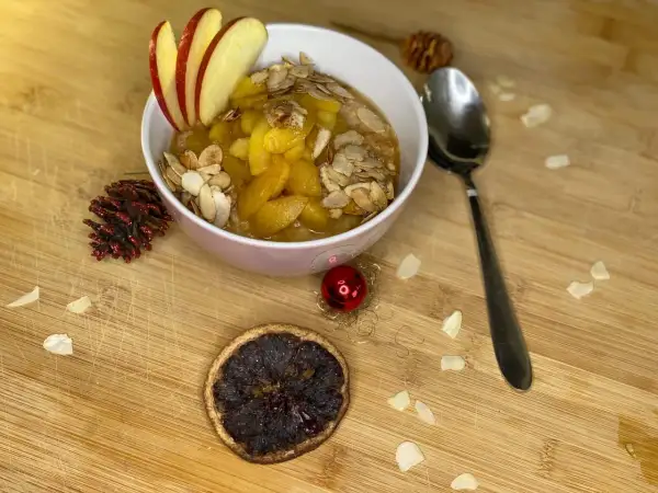 Schüssel mit Bratapfel Porridge, garniert mit Apfelscheiben und Mandelblättchen. Ein festlicher Genuss für kalte Tage.