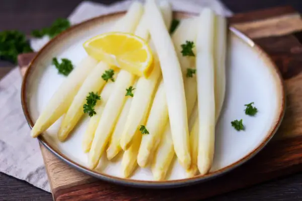 Frischer weißer Spargel, perfekt gekocht, garniert mit Petersilie und einer Zitronenspalte auf einem Teller. Ein Genuss, wenn Spargel Saison hat.