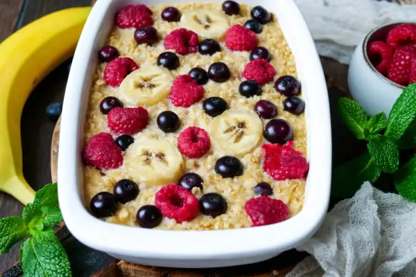 Leckere instant oats rezepte: gebackener Haferbrei mit Bananen, Himbeeren und Blaubeeren, garniert mit frischer Minze.