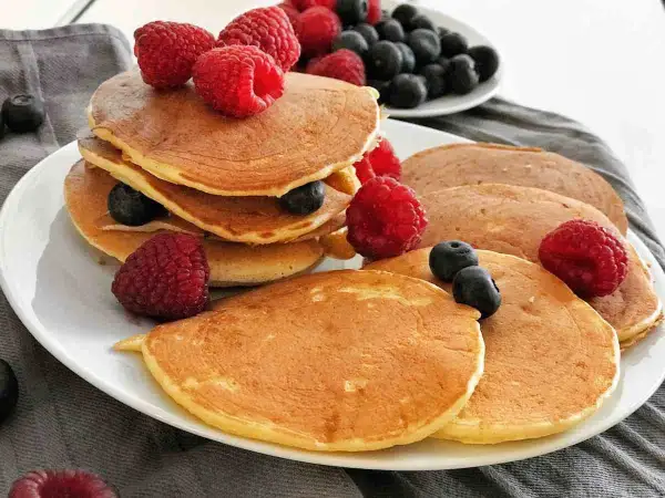 Gestapelte, goldbraune, gesunde Pancakes mit frischen Himbeeren und Blaubeeren garniert. Ein köstlicher Start in den Tag.