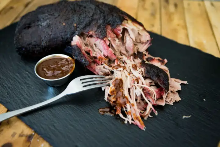 Saftiges Pulled Pork, perfekt für ein gerupftes Rezept. Eine Gabel nimmt zarte Fleischfasern auf, daneben eine Schale BBQ-Sauce.